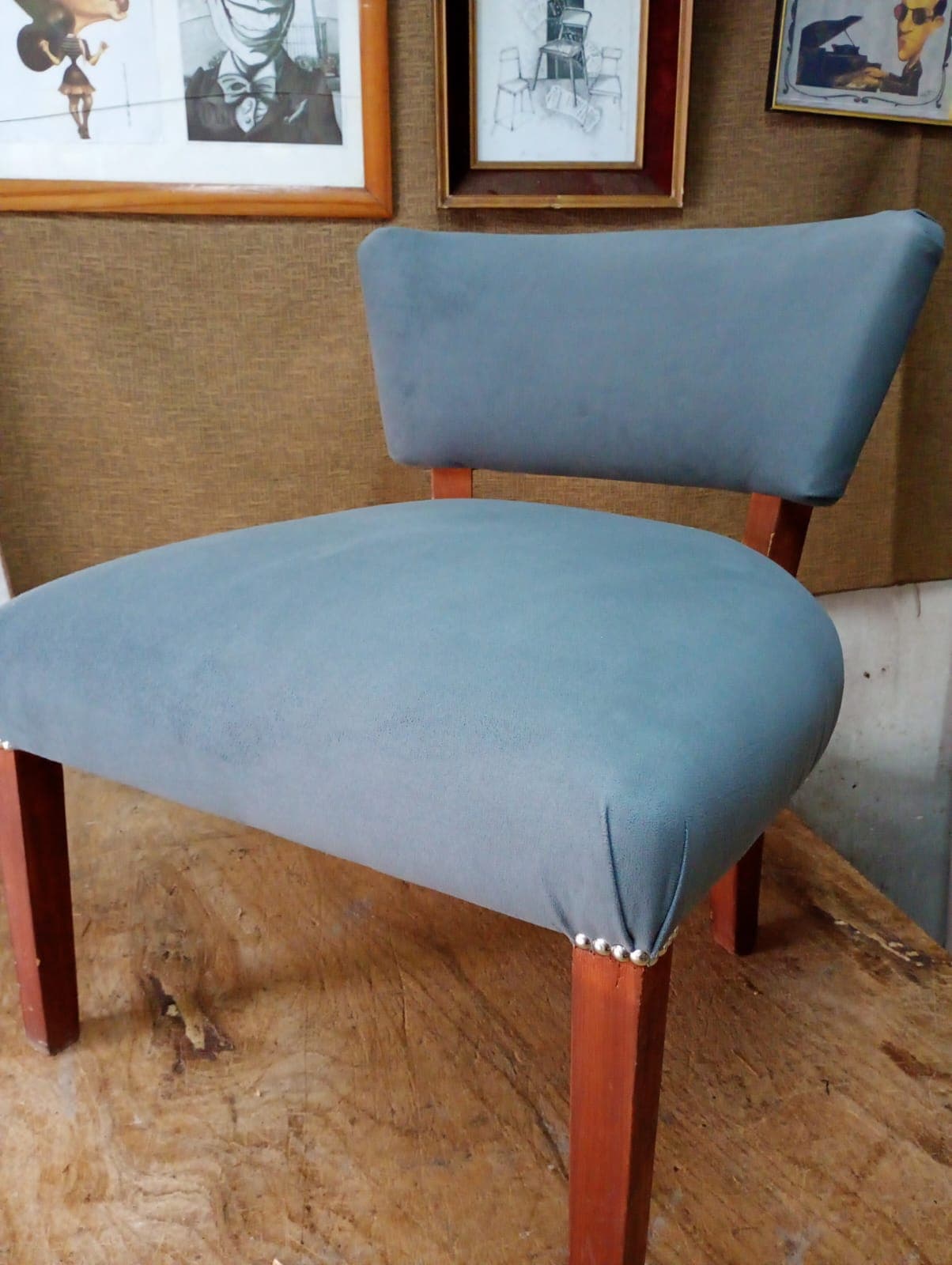 Sillón matero bajo tapizado en tela gris azulada, con respaldo curvo y patas de madera